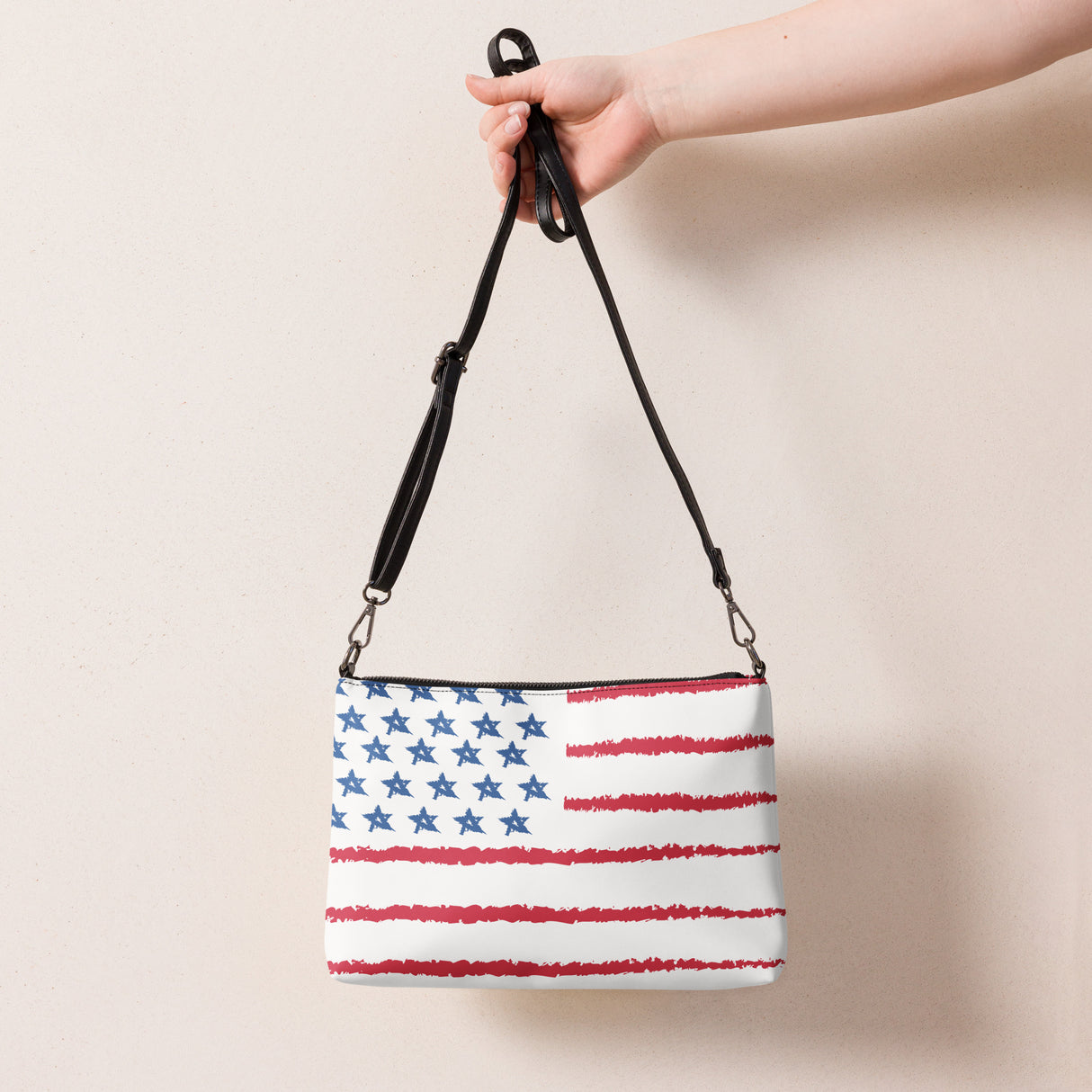 Mini leather crossbody purse with American flag design and adjustable black strap held by hand