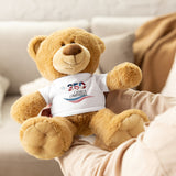 Plush teddy bear and person holding it wearing a white 250 years anniversary t-shirt on couch